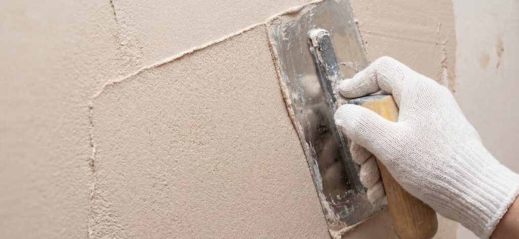 Ein Verarbeiter trägt COLORIAMO Marmorputz mit einer Glättkelle auf eine Wand auf, für stilvolle Wandgestaltung.