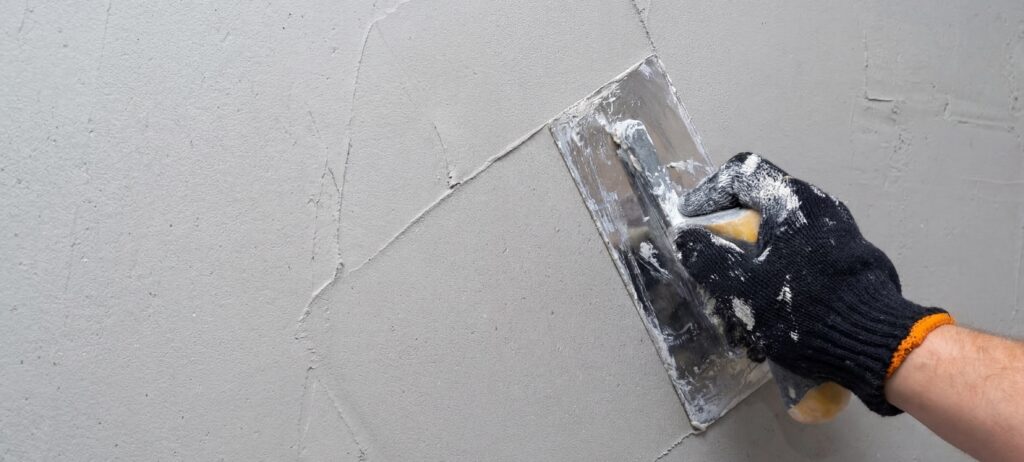 Ein Handwerker verarbeitet Kalkputz mit einer Glättkelle für eine fugenlose Wandgestaltung im Badezimmer. | © COLORIAMO