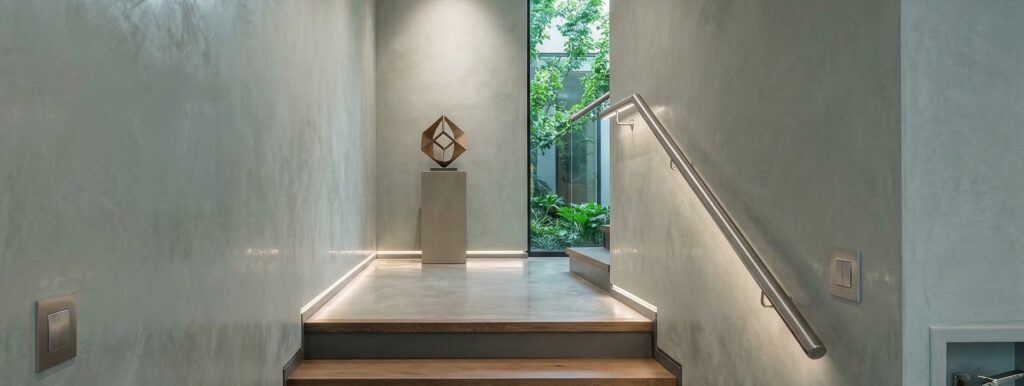 Elegante Wandgestaltung im Treppenhaus mit Metallspachtel und Sichtbeton von COLORIAMO. | © COLORIAMO